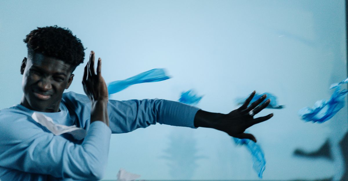 A man shields himself from flying plastic waste indoors.