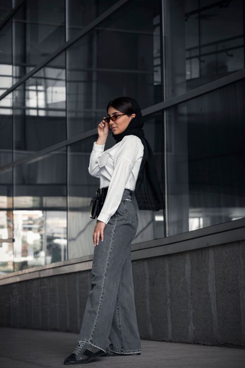 Free A fashionable woman in hijab and sunglasses posing by a modern glass building in Tehran, Iran. Stock Photo