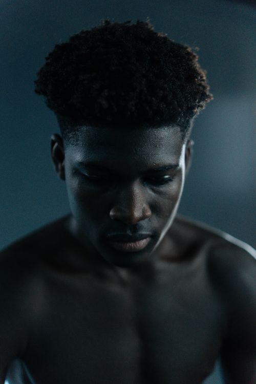 Free A shirtless young man with afro hair appears thoughtful and introspective in a dimly lit studio setting. Stock Photo