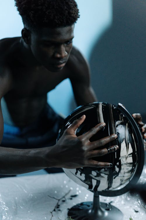 A Topless Man Holding a Globe with Black Liquid