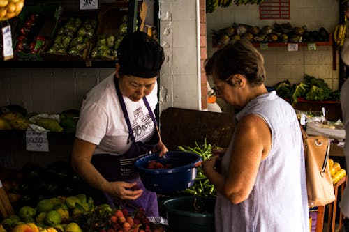 Foto De Mujer Sosteniendo Un Cubo Azul Y Una Mujer Mirando Hacia La Fruta Vestida Con Camisa Azul Sin Mangas