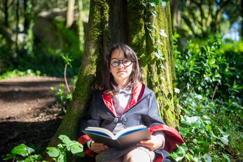 Free Young girl in costume reading a book under a tree, enjoying a magical outdoor setting Stock Photo