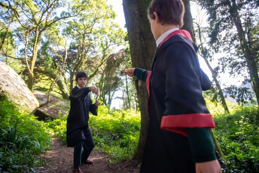 Children dressed as wizards playing with magic wands in a lush forest setting, capturing a whimsical fantasy moment.