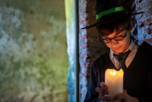 A young boy in a wizard costume holding a lit candle with a mysterious expression.