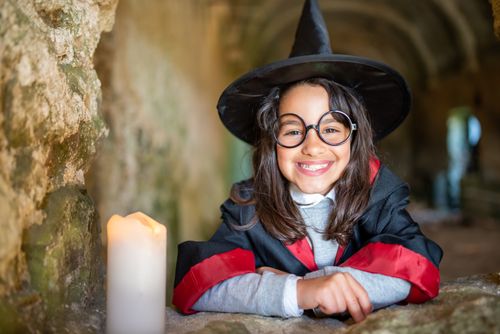 Free Smiling girl in witch costume with candle, set in ancient stone hallway, evokes magical charm. Stock Photo