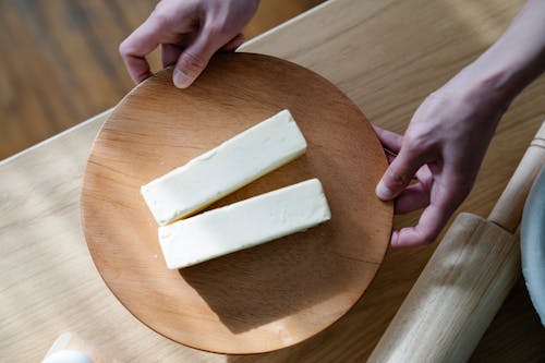 Close-Up Shot of a Person Holding a Wooden Plate with Sliced Butters