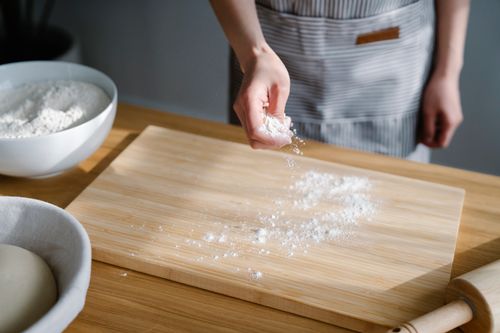 Free Close-up of a baker sprinkling flour on a wooden board in a kitchen setting. Stock Photo
