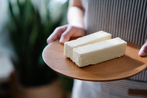 Free Close-up of hands holding a wooden plate with two sticks of butter. Stock Photo