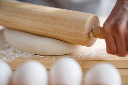 Close Up Photo of a Person Kneading Dough with a Rolling Pin