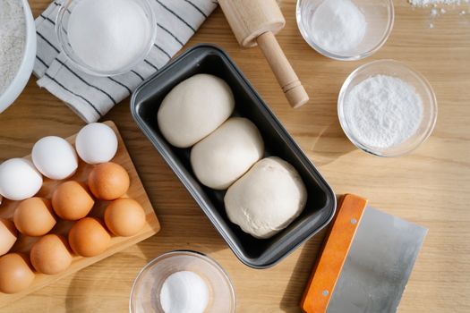Flat lay of baking ingredients including dough, eggs, and flour on a wooden table, perfect for culinary projects.