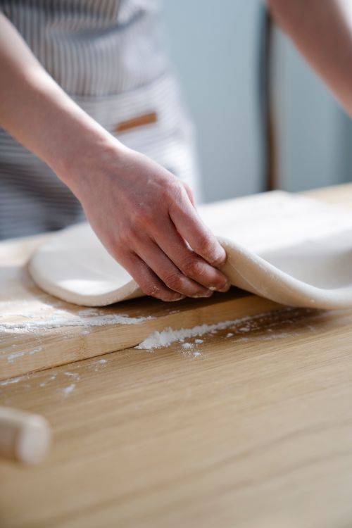 Free Close-up of hands shaping dough on a wooden kitchen counter, ideal for baking themes. Stock Photo