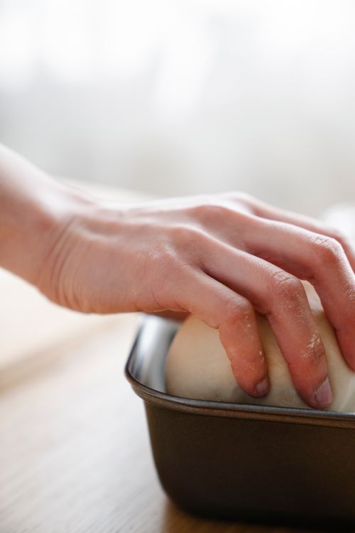 Free A hand gently kneading dough in a baking pan, showcasing hands-on baking preparation. Stock Photo