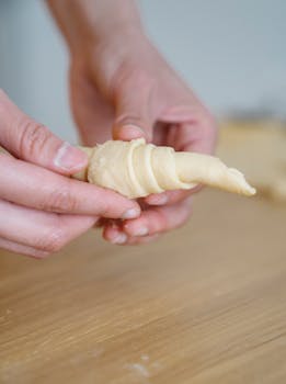 A close-up image of hands rolling pastry dough on a wooden surface, perfect for baking or cooking themes.