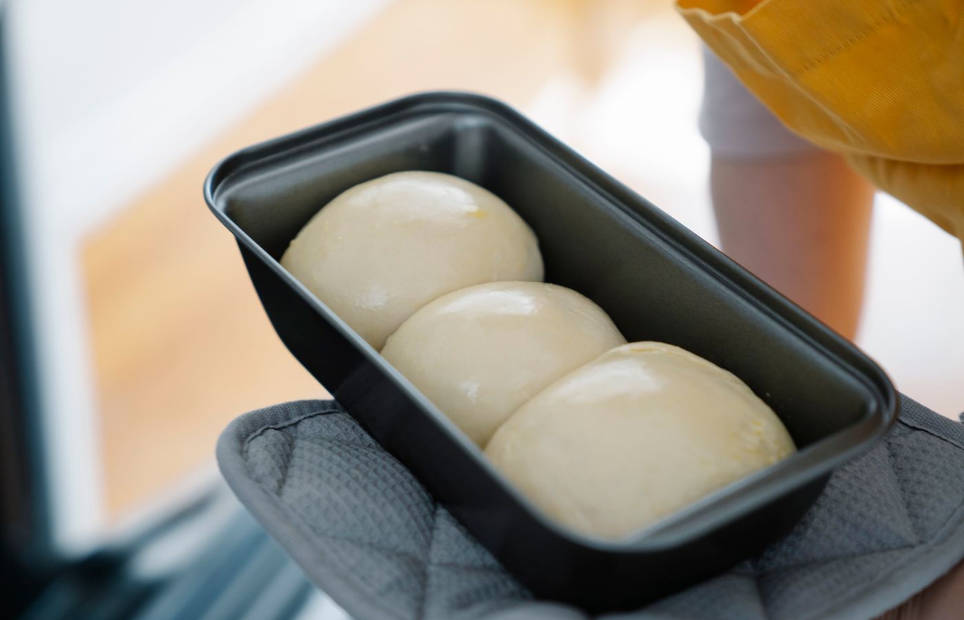 Close-up of dough balls in a baking tray held with an oven mitt, ready for baking.