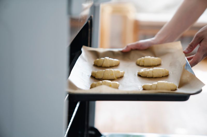 Baker placing golden butter croissants onto a pastry tray