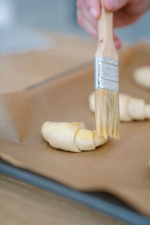 Free Close-up of a hand brushing croissants with butter on a baking sheet. Stock Photo