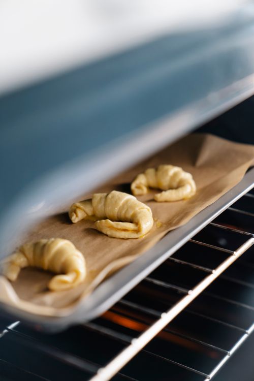Free Three croissants baking on parchment paper in an oven, showcasing fresh pastries. Stock Photo