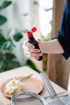A person holding a sauce bottle in a kitchen setting, preparing to cook or garnish food.