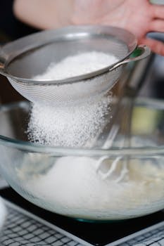 Close-up of flour being sifted into a mixing bowl, ideal for baking projects.
