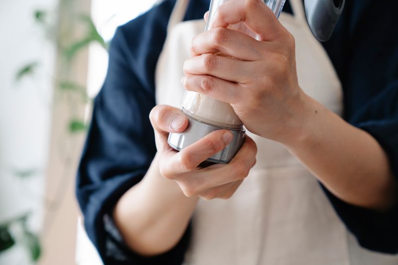 A person wearing an apron holds and shakes a protein shaker indoors