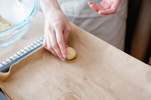 Free Close-up of hand carefully shaping dough ball on baking sheet with parchment paper. Stock Photo