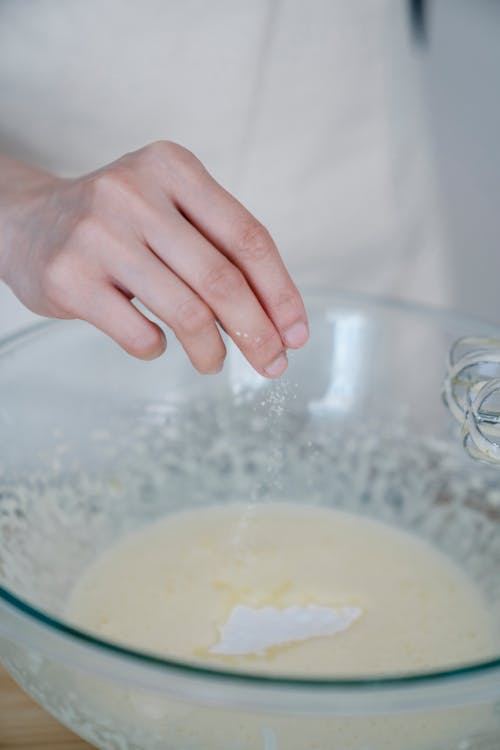 A Person Sprinkling Salt on Dough Mixture