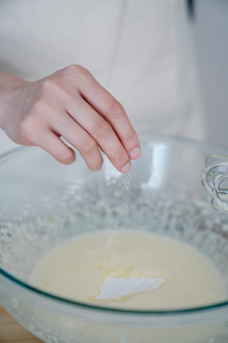 A Person Sprinkling Salt On Dough Mixture