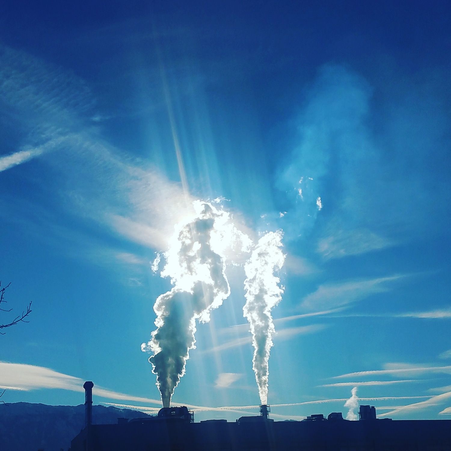 Silhouette of an industrial plant with steam emissions in a bright, clear sky.