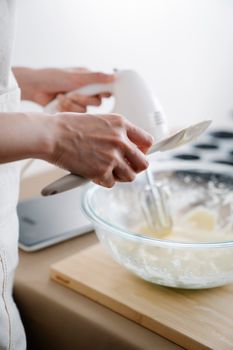 Close-up of hands using an electric mixer to mix dough in a glass bowl on a wooden board.