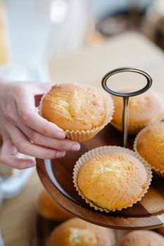 A person taking a freshly baked cupcake from a wooden tray, showcasing baking skills.