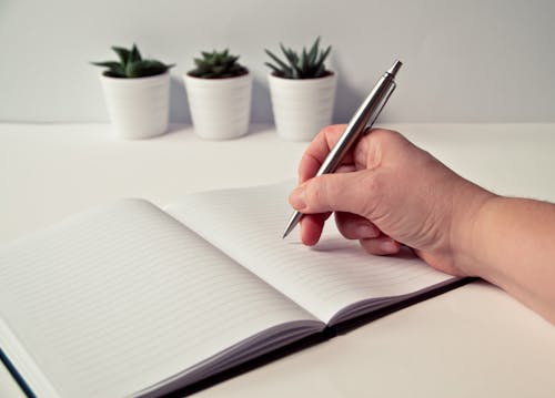 Free Person Holding Silver Retractable Pen in White Ruled Book Stock Photo