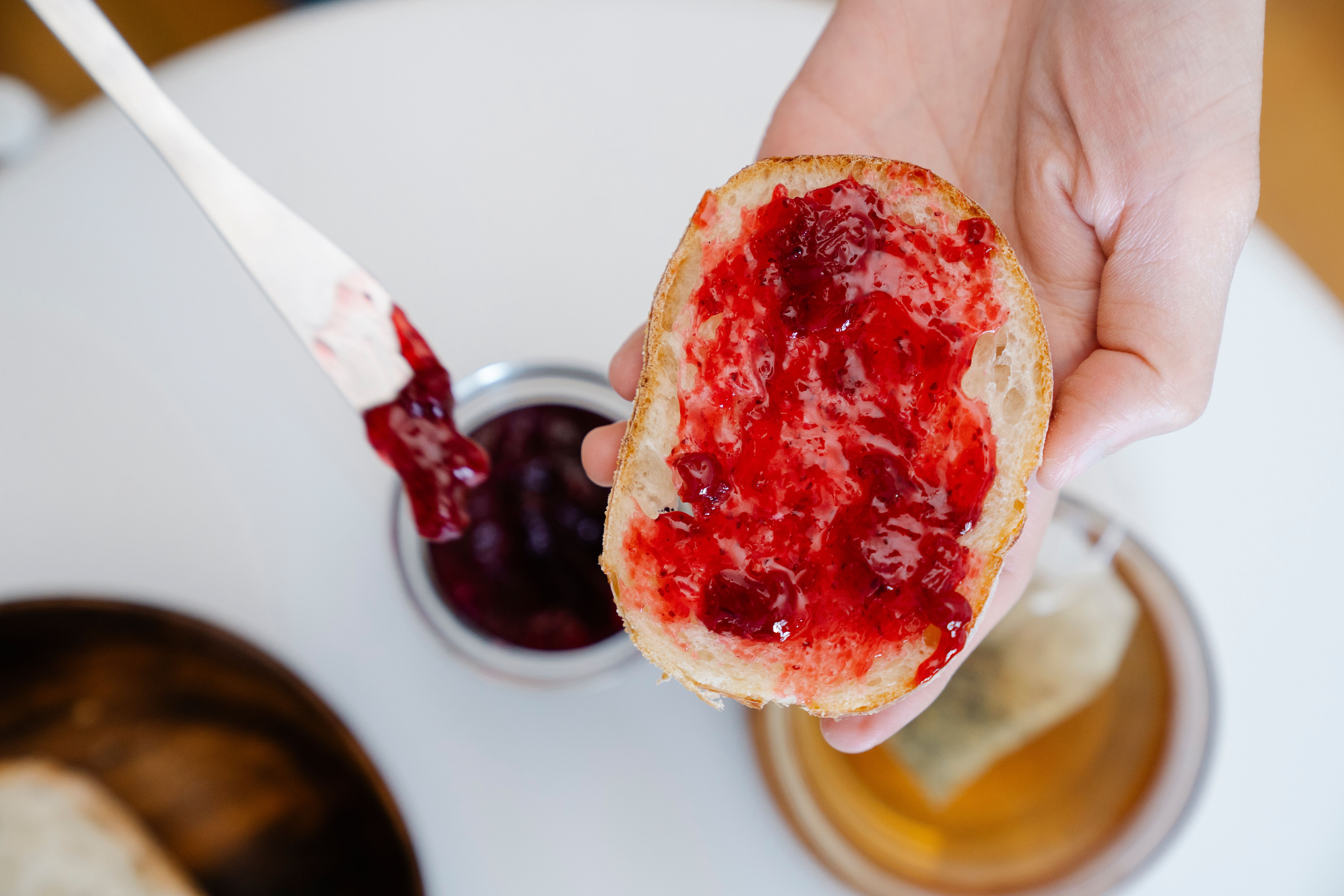 Close-up of hand holding bread with strawberry jam spread over it.