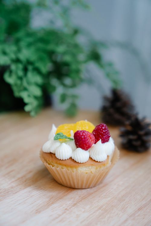 Free A close-up of a cupcake topped with whipped cream, raspberries, and orange slices. Stock Photo