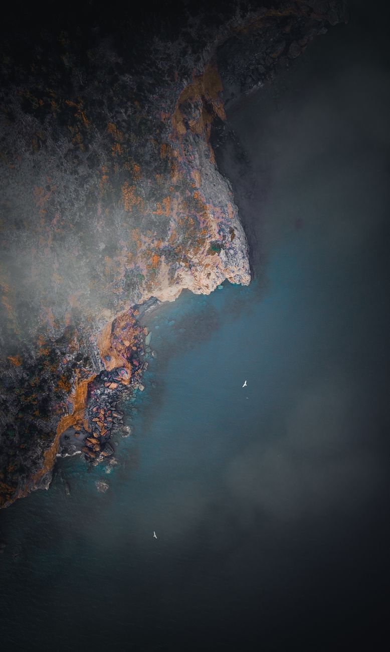 Drone view of picturesque scenery of rocky formations near calm sea under haze in summer evening
