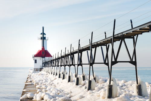 Red and White Concrete Lighthouse Surrounded by Snow Near Body of Water