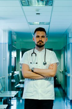 A medical professional with a stethoscope stands confidently in a hospital hallway.