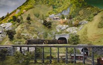 立体模型描绘了一列火车模型穿过风景优美的乡村景观，行驶在桥梁上