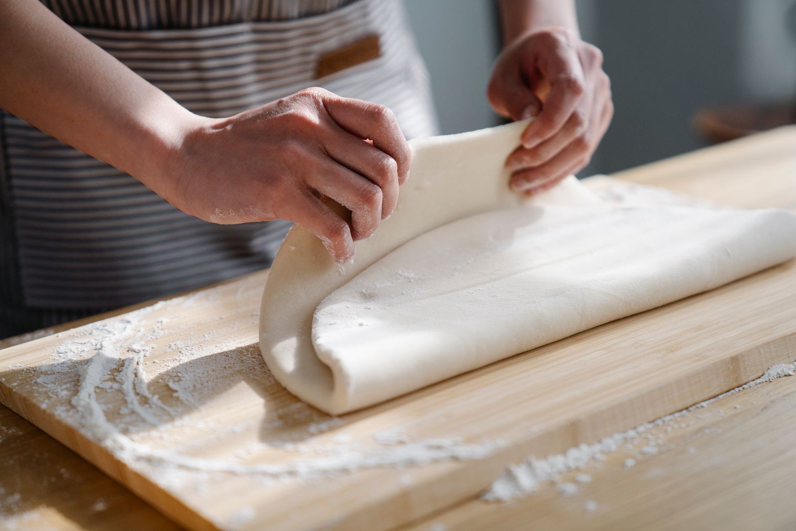 Hands folding dough on a floured wooden surface
