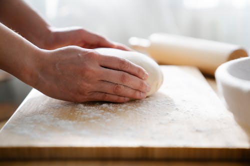 Close Up Shot of a Person Holding Dough on Wooden Board