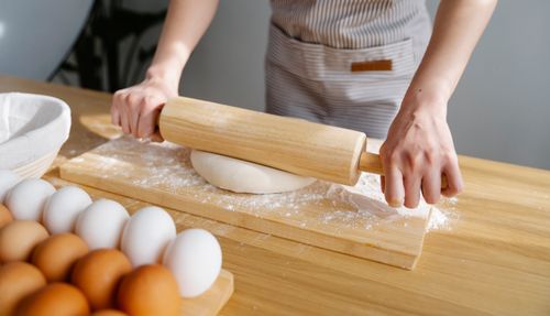 Free Close-up of a person kneading dough with a rolling pin, surrounded by eggs, on a wooden board in natural light. Stock Photo