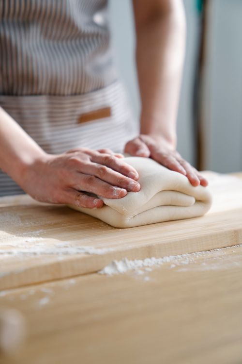 Free Close-up of a person folding dough on a flour-dusted wooden surface. Stock Photo