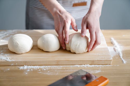 Person Holding Dough on a Wooden Chopping Board