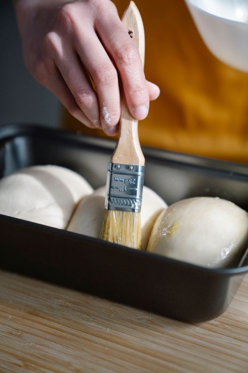 Free Close-up of a hand brushing dough with egg wash in a baking pan, preparing for baking. Stock Photo