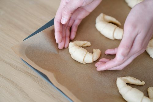 Free Close-up of hands arranging croissant dough on a baking tray lined with paper. Stock Photo