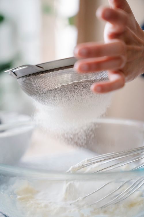 Free Close-up of a hand sifting flour into a bowl during baking preparation. Stock Photo