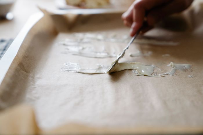 Hand spreading butter on a baking tray lined with parchment paper