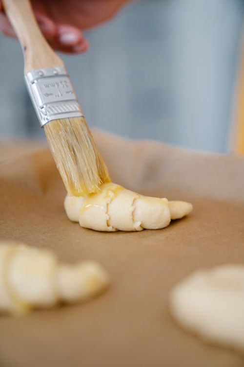 Free Close-up of a hand applying egg wash to pastry dough on parchment paper. Stock Photo