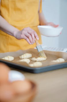 A person applying egg wash to croissants on a baking tray, enhancing the golden finish.