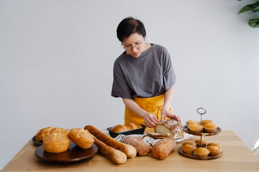 A woman wearing an apron slices freshly baked bread on a wooden table.