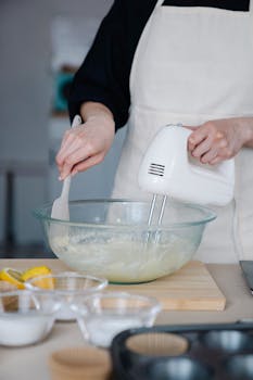 Hands preparing cake batter with a mixer in a kitchen setting.